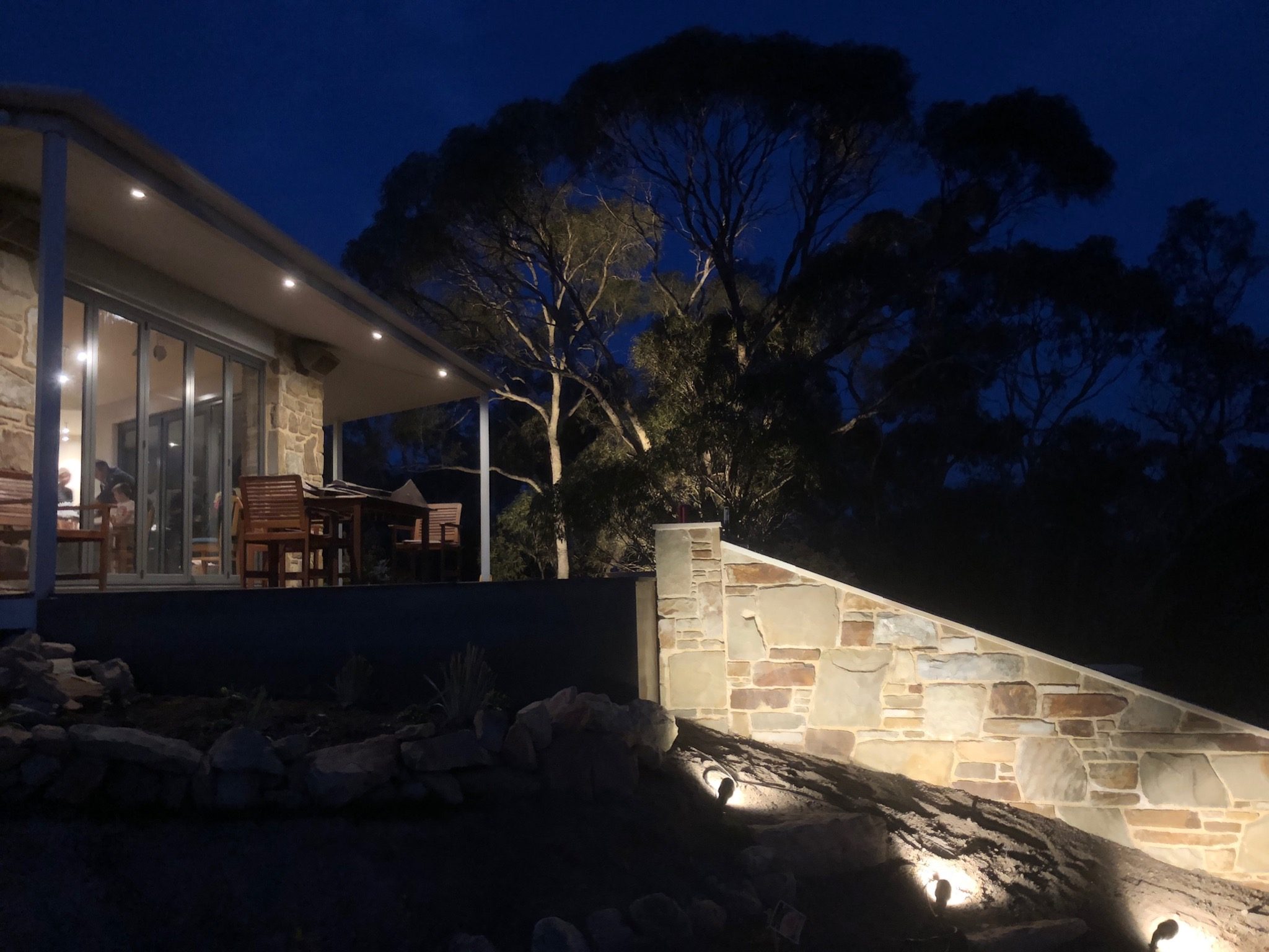 Stone retaining wall with outdoor lighting beside a landscaped home and entertaining.